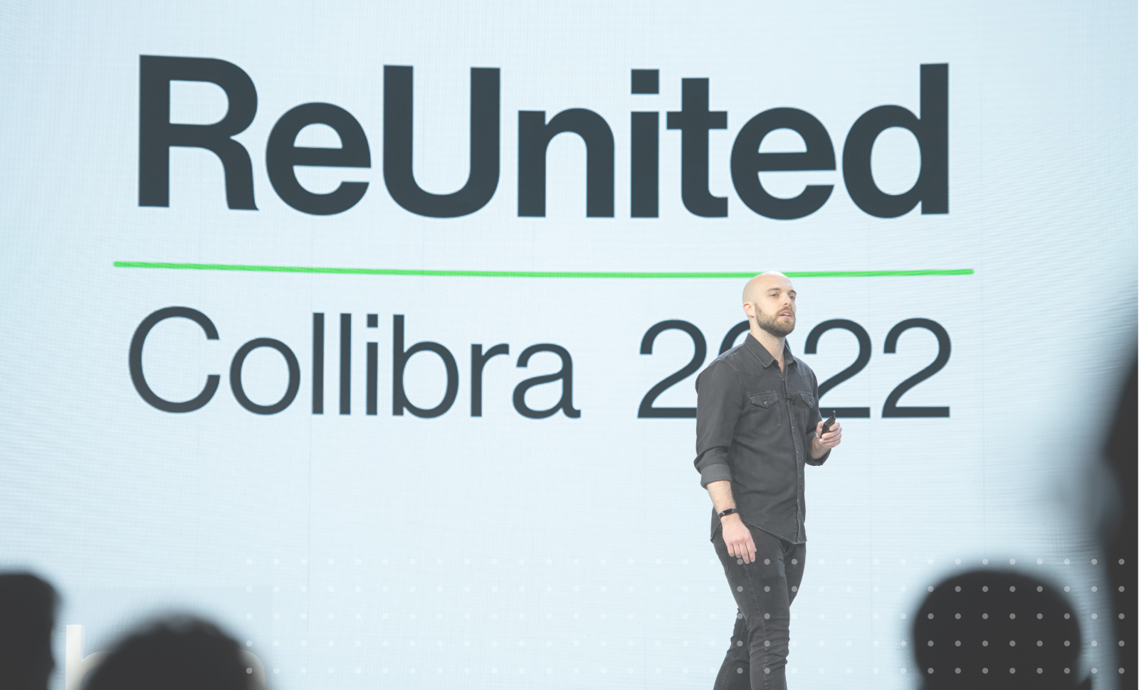 科迪·施洛特在舞台上展示了一个屏幕，上面写着“团聚的Collibra 2022”新万博移动客户端