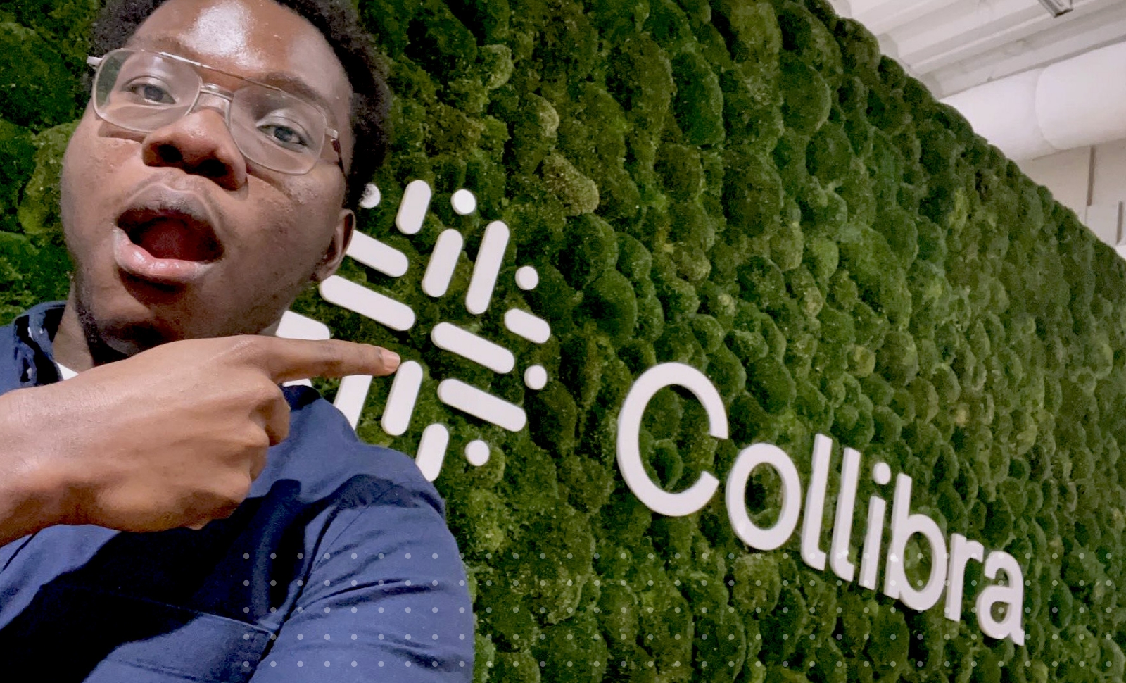 新万博移动客户端Collibra实习生Sam Mensah用手指指着带有Collibra大标志的活墙。